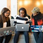 Three women working together on laptops in a casual office setting, emphasizing teamwork and collaboration.