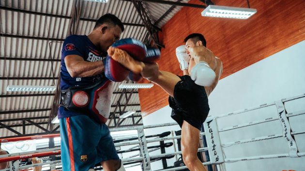Two fighters engage in a dynamic Muay Thai training session inside a gym.