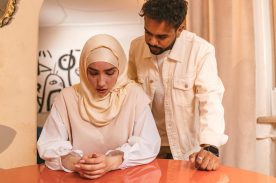 A man comforts a woman in a hijab indoors, providing emotional support and empathy.